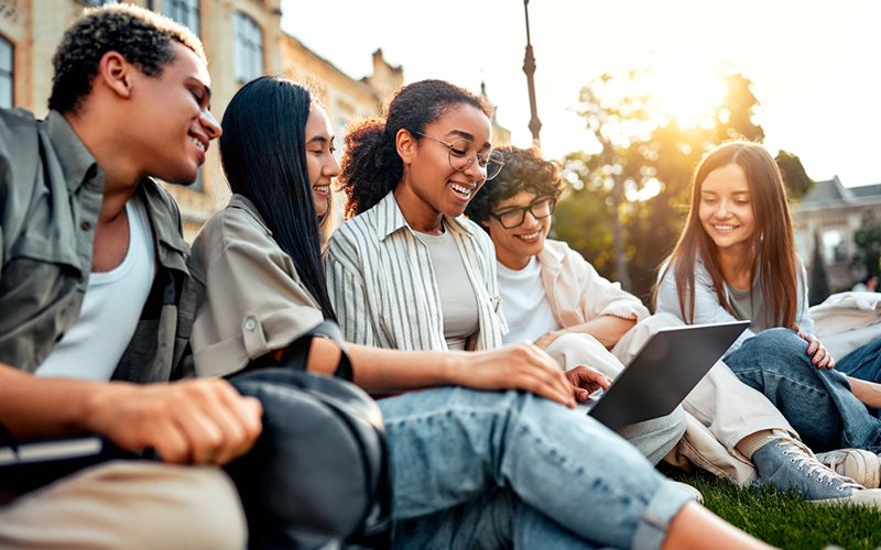 College students sitting on grass on campus socializing, studying and spending time at leisure.